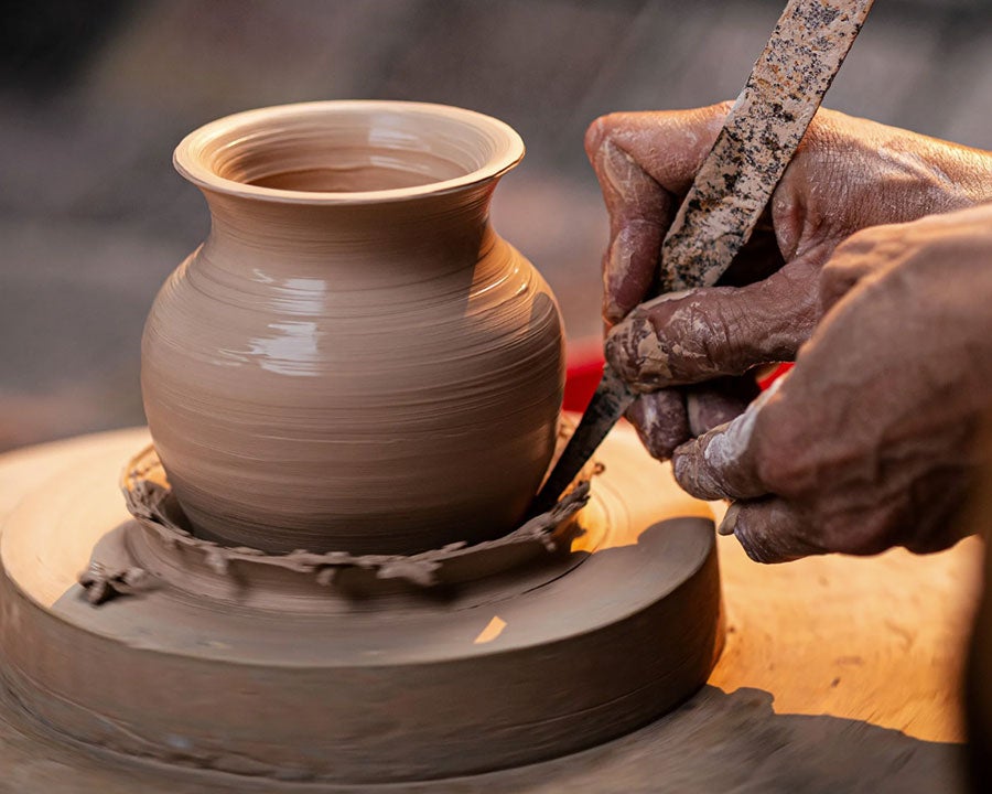 Someone cutting clay off the bottom of a pot in a ceramics 3 class
