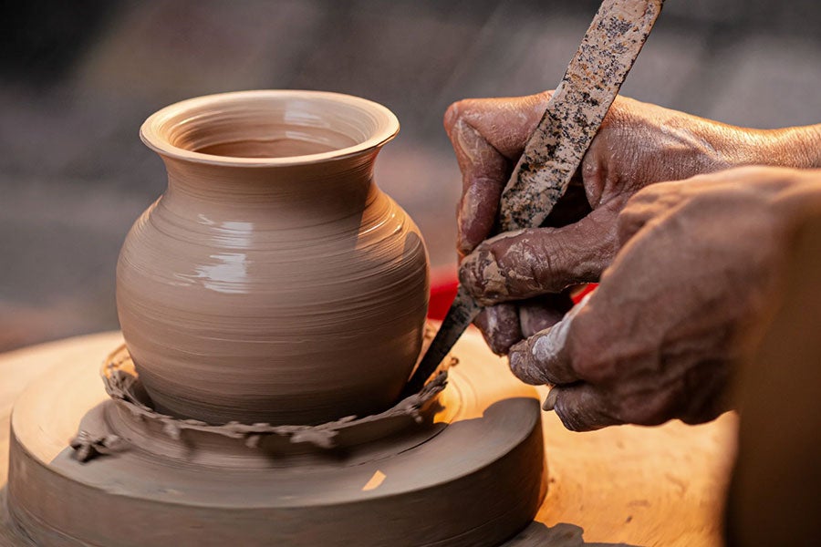 Someone cutting clay off the bottom of a pot in a ceramics 3 class